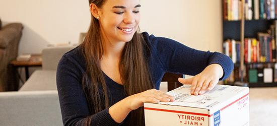 年轻女子给美国邮政优先邮件国际包裹贴上标签.